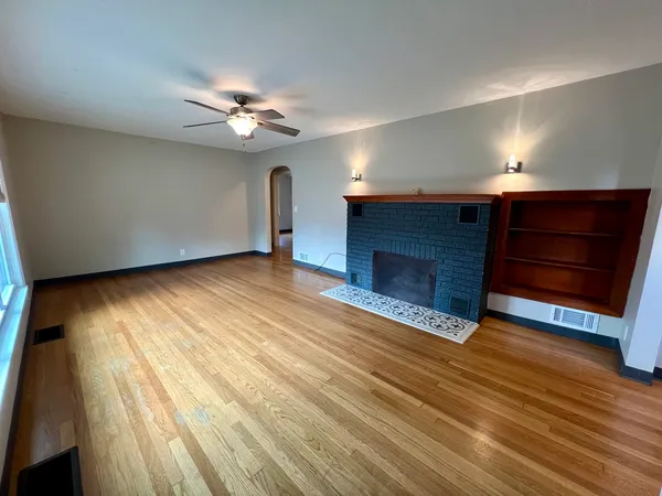 a view of an empty room with wooden floor fireplace and a window