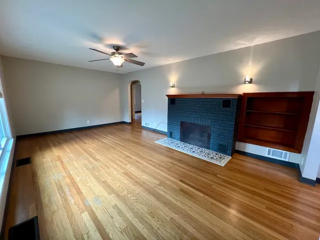 a view of an empty room with wooden floor fireplace and a window