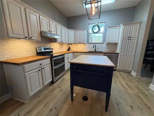 a kitchen with stainless steel appliances granite countertop a refrigerator a sink dishwasher a stove and white countertops with wooden floor