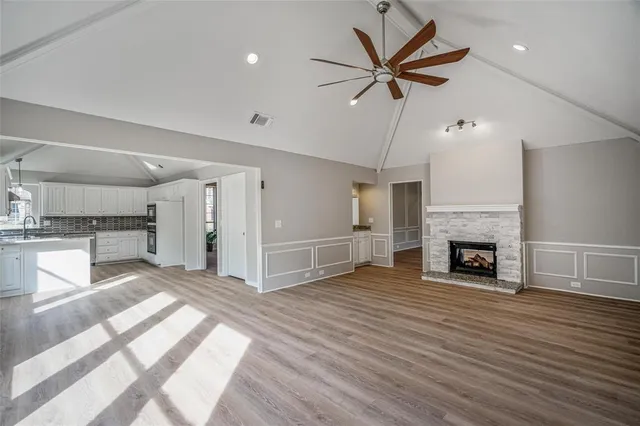 a view of a livingroom with a fireplace a ceiling fan and a kitchen view