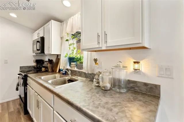 a kitchen with a sink dishwasher and white cabinets with wooden floor