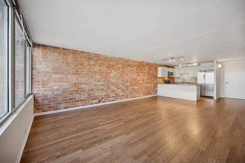 a view of empty room with wooden floor and kitchen view