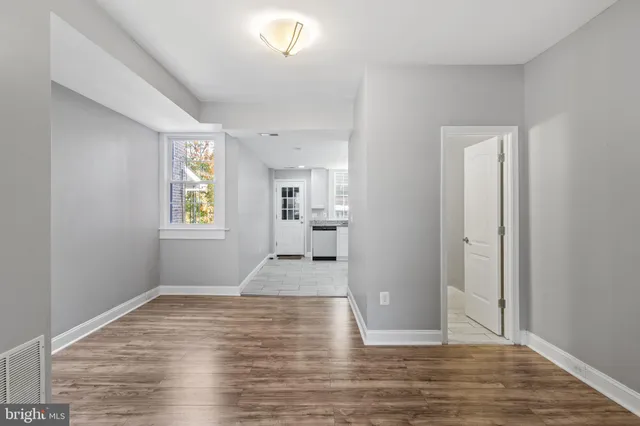 a view of empty room with wooden floor and kitchen view