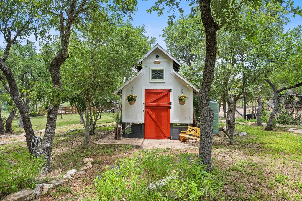 290 Sunset Ridge Dripping Springs, TX 78620 - Photo 35 of 37 A charming outbuilding with bright red barn doors adds character to the verdant landscape.