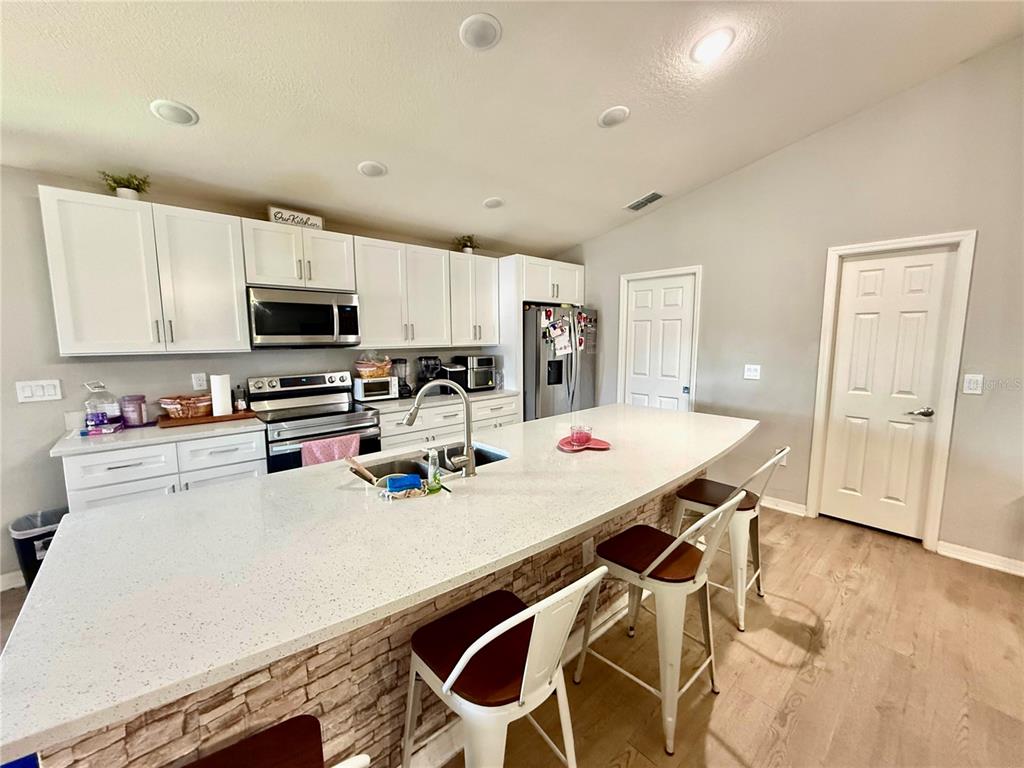 4098 Ruby Run Haines City, FL 33844 - Photo 18 of 34 a kitchen with stainless steel appliances a stove a sink a microwave a refrigerator a stove and white cabinets with wooden floor