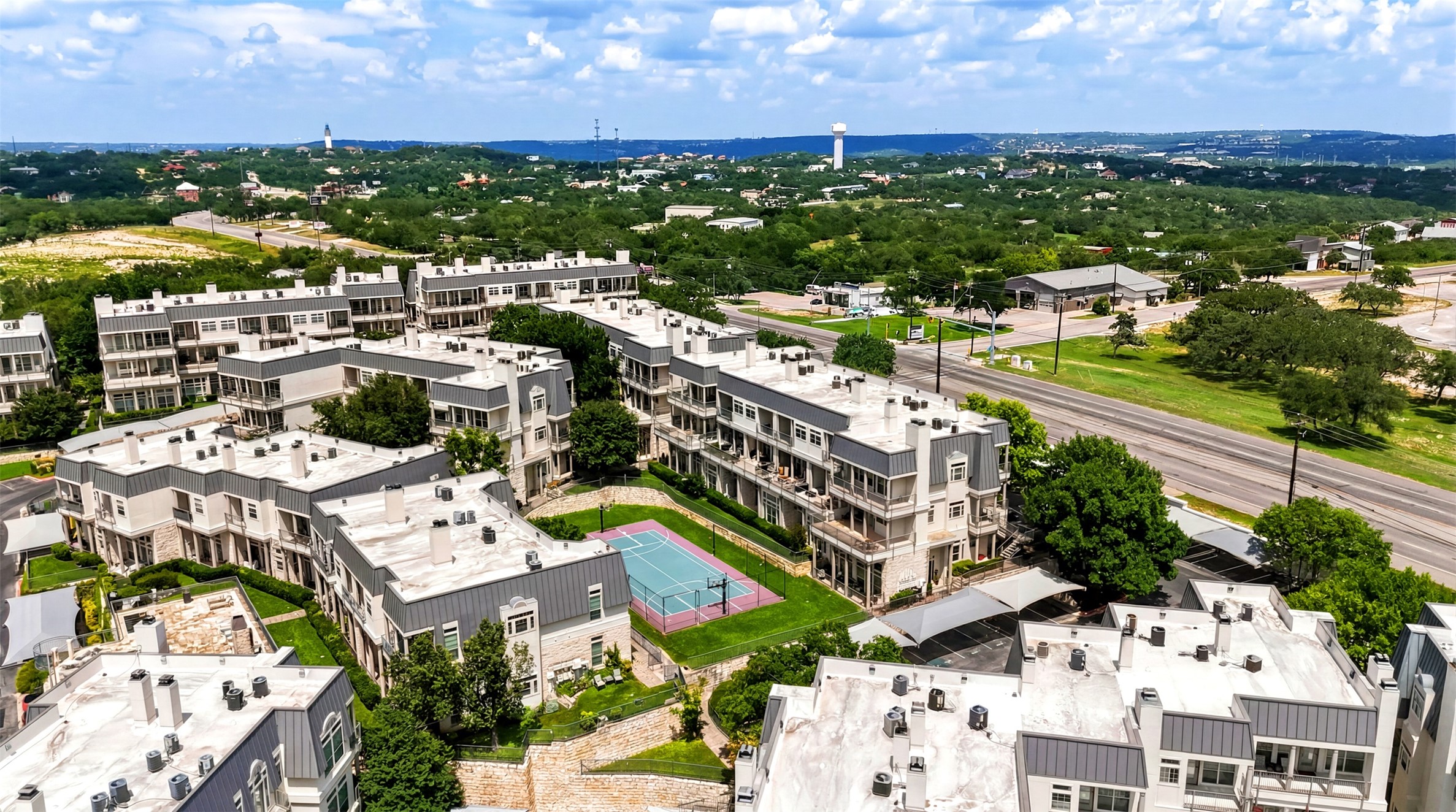 2918 Ranch Road 620, Unit 265 Austin, TX 78734 - Photo 5 of 40 An aerial perspective reveals a vibrant community nestled among verdant hills, featuring multi-story residences and a shared recreational court.