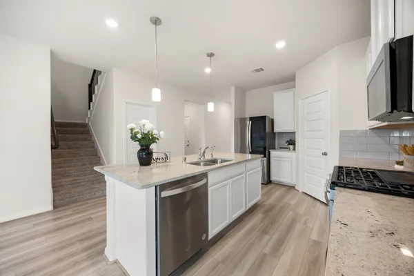 a kitchen with a sink stainless steel appliances a counter top space cabinets and wooden floor