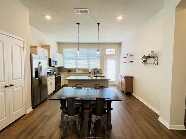 a kitchen with stainless steel appliances a dining table chairs stove refrigerator and cabinets
