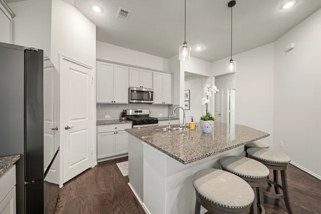 a kitchen with stainless steel appliances granite countertop a sink a refrigerator a stove a dining table and chairs with wooden floor