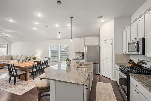 a kitchen with stainless steel appliances granite countertop sink stove refrigerator dining table and chairs