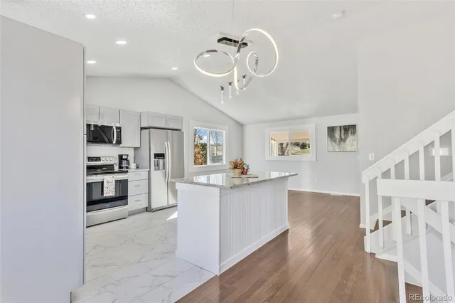 a kitchen with stainless steel appliances a stove top oven a sink dishwasher and a refrigerator with wooden floor