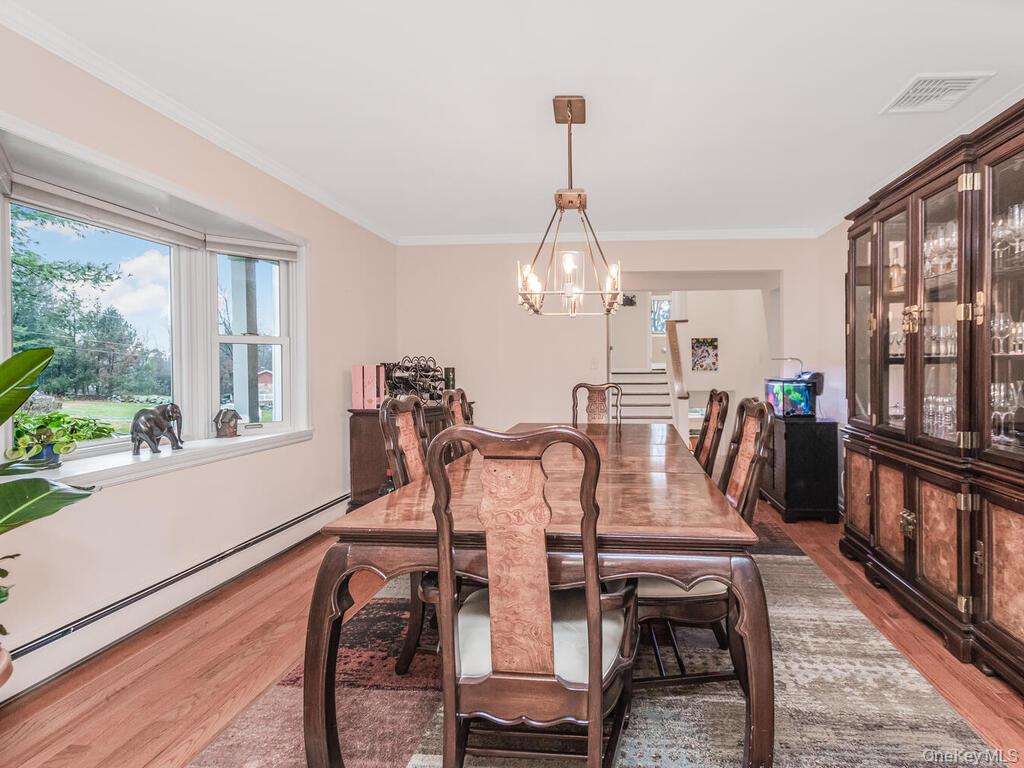 70 Breckenridge Road Mahopac, NY 10541 - Photo 6 of 29 Dining room featuring baseboard heating, a chandelier, light wood-style flooring, healthy amount of natural light, and crown molding