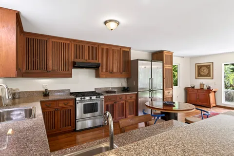 a kitchen with stainless steel appliances granite countertop a stove a sink dishwasher and a refrigerator with wooden cabinets