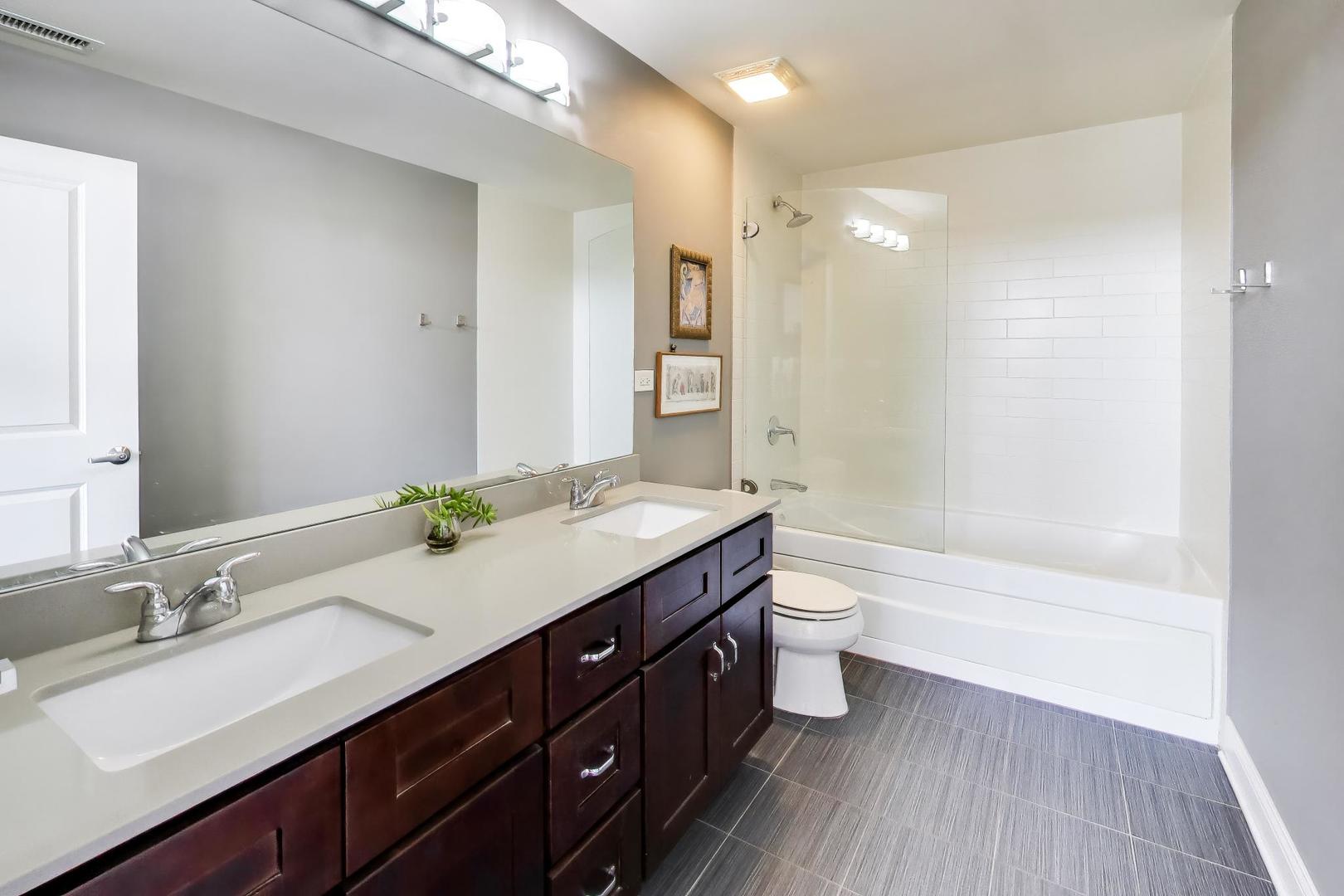 4846 North Clark Street, Unit 510 Chicago, IL 60640 - Photo 20 of 32 a bathroom with a granite countertop sink toilet a large mirror a bathtub and shower