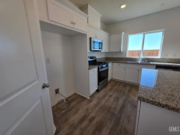 a kitchen with granite countertop a sink a stove top oven and cabinetry
