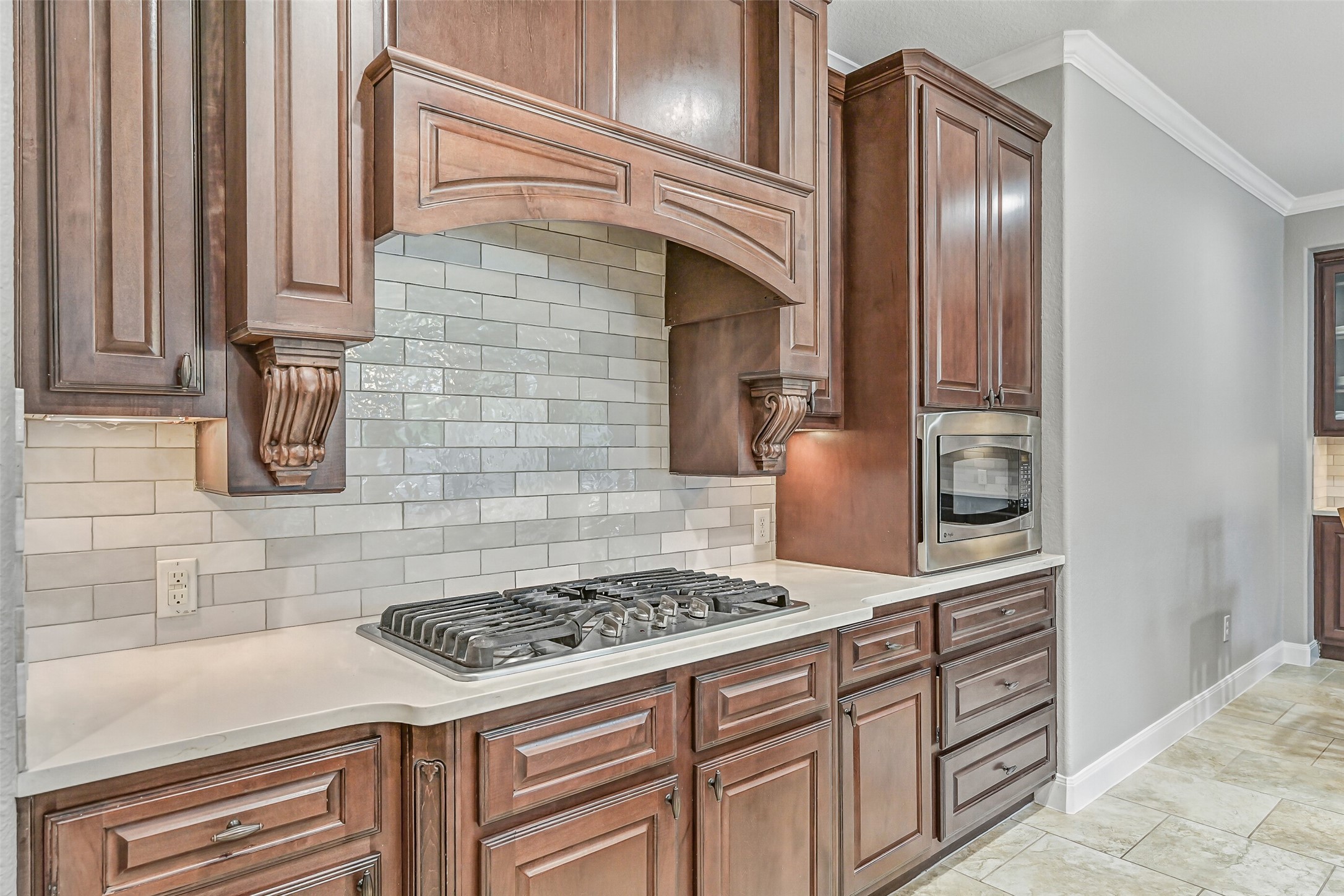 1008 Point Isabel Lane Friendswood, TX 77546 - Photo 16 of 50 The 5 burner gas cooktop is set beneath a custom vent hood with decorative trim, surrounded by tile backsplash and ample counter space, complete with pots & pans drawers, creating a well organized cooking area.