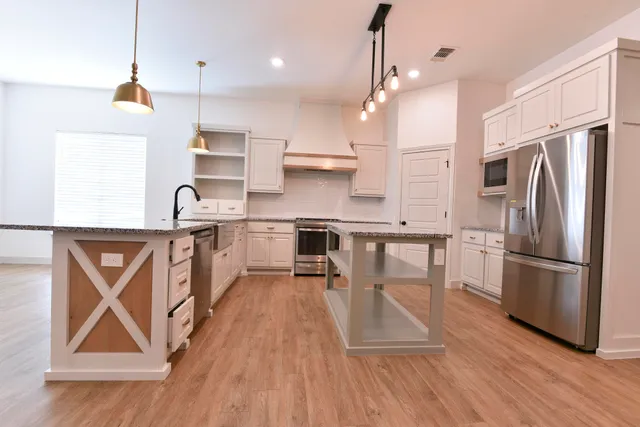 a kitchen with stainless steel appliances a refrigerator a sink dishwasher a stove and white cabinets with wooden floor