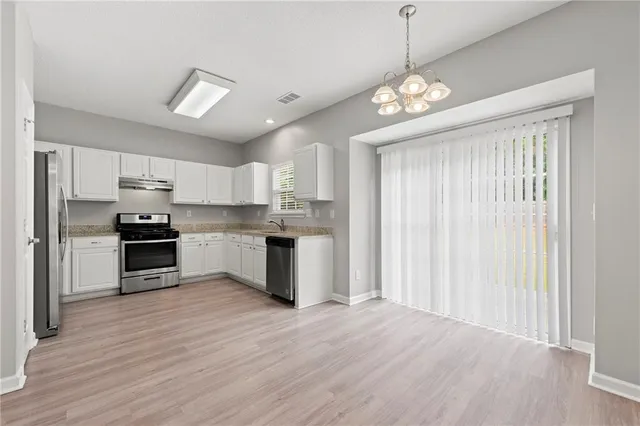 a kitchen with stainless steel appliances granite countertop a refrigerator a sink dishwasher a stove and white cabinets with wooden floor