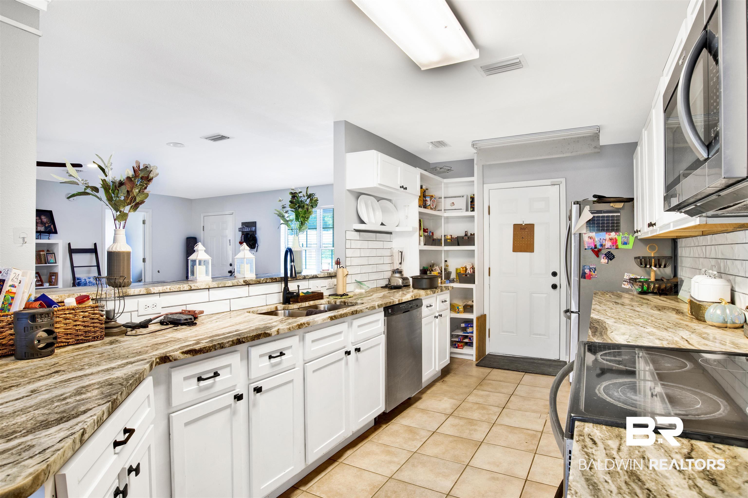 24384 Sailfish Lane Orange Beach, AL 36561 - Photo 8 of 23 Kitchen with backsplash, appliances with stainless steel finishes, light stone counters, light tile patterned floors, and sink