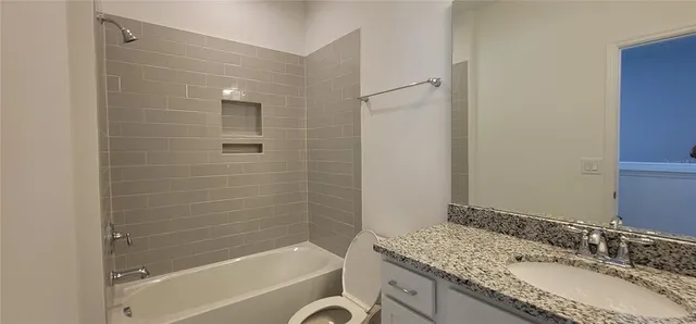 a bathroom with a granite countertop bathtub shower sink vanity and a toilet