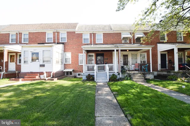 a view of a brick house with a yard plants and large tree
