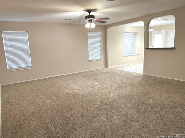 an empty room with a chandelier fan and windows