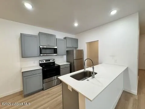 a kitchen with stainless steel appliances a sink dishwasher a stove top oven a refrigerator with grey cabinets and wooden floor