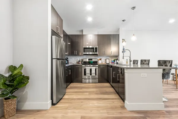 a kitchen with stainless steel appliances granite countertop a refrigerator a sink dishwasher a stove and a dining table with wooden floor