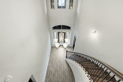 24714 Longwood Forest Drive Spring, TX 77373 - Photo 4 of 21 This photo showcases a spacious, well-lit foyer with high ceilings, elegant chandelier, and a curved staircase with wrought iron railing. The large windows and wood flooring add a touch of sophistication and warmth.