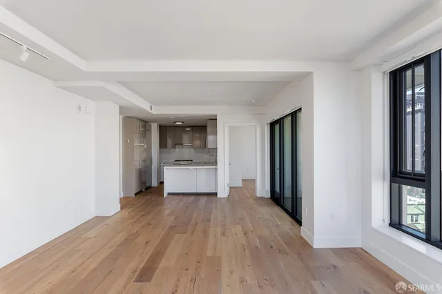 a view of a hallway to room with window and wooden floor