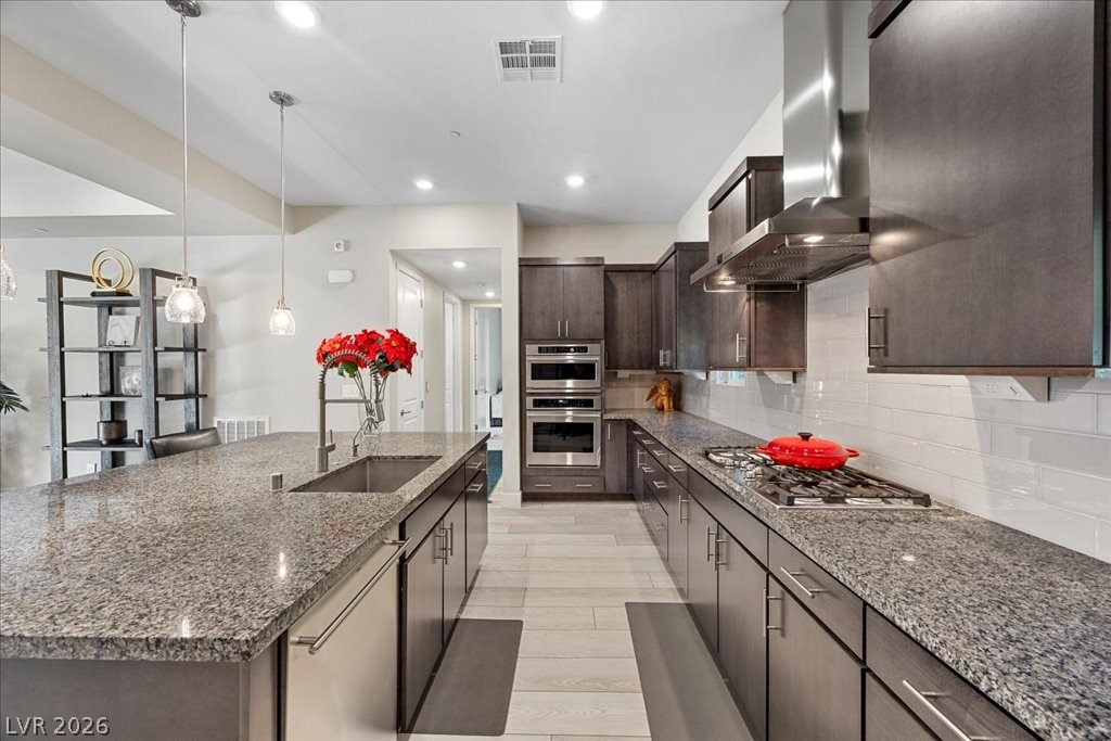 4262 Swift Street Las Vegas, NV 89135 - Photo 16 of 75 Kitchen with dark stone countertops, pendant lighting, wall chimney exhaust hood, a large island, and appliances with stainless steel finishes