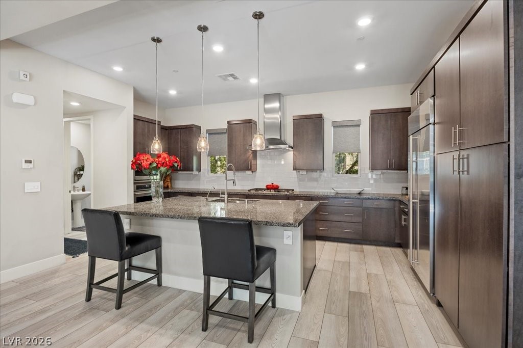 4262 Swift Street Las Vegas, NV 89135 - Photo 17 of 75 Kitchen featuring a kitchen bar, hanging light fixtures, dark stone counters, a kitchen island with sink, and light wood-style floors