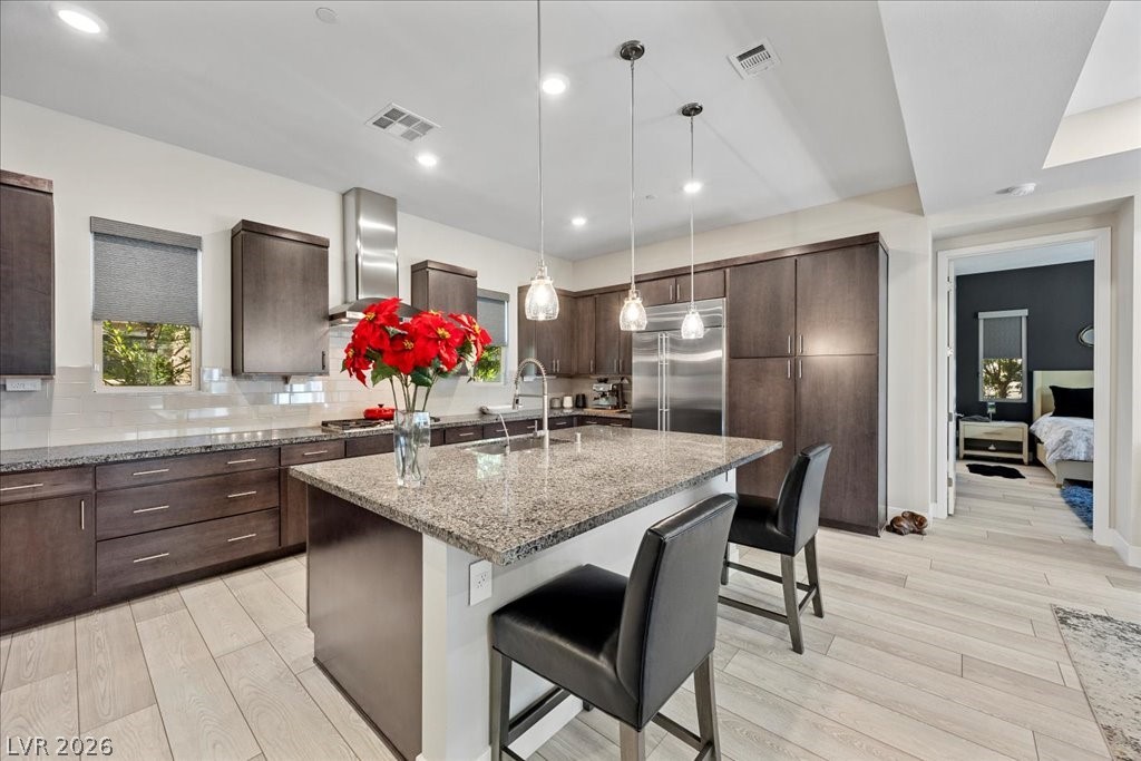 4262 Swift Street Las Vegas, NV 89135 - Photo 19 of 75 Kitchen with a breakfast bar area, dark brown cabinets, light stone counters, decorative light fixtures, and an island with sink