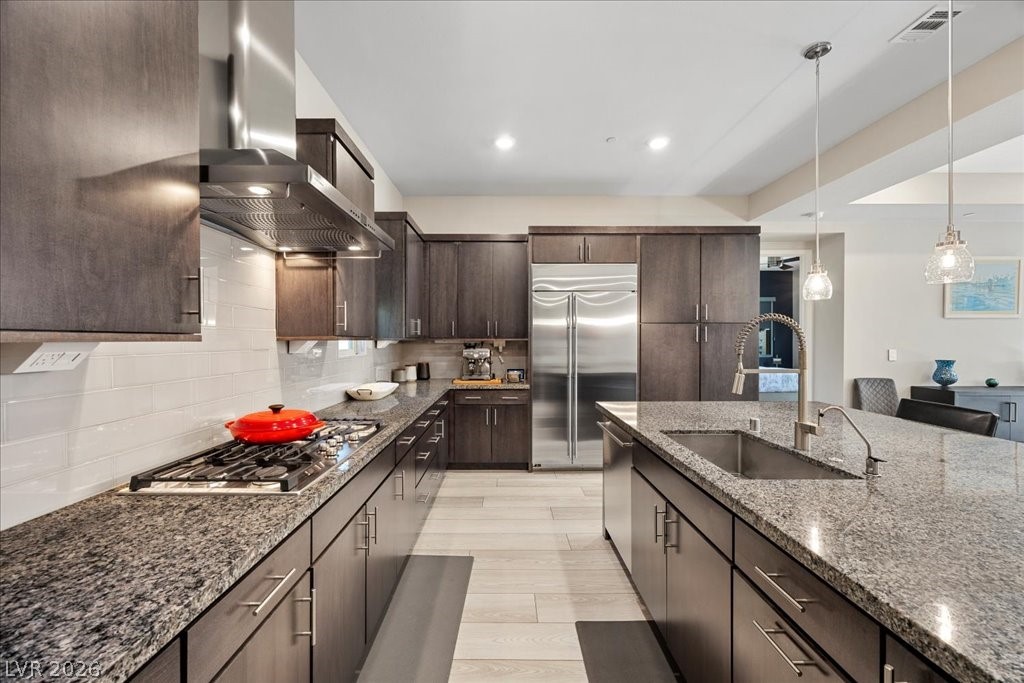 4262 Swift Street Las Vegas, NV 89135 - Photo 22 of 75 Kitchen with dark brown cabinetry, wall chimney range hood, dark stone countertops, stainless steel appliances, and decorative backsplash