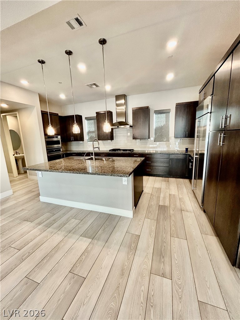 4262 Swift Street Las Vegas, NV 89135 - Photo 63 of 75 Kitchen with tasteful backsplash, hanging light fixtures, dark stone countertops, a kitchen island with sink, and light wood-style floors
