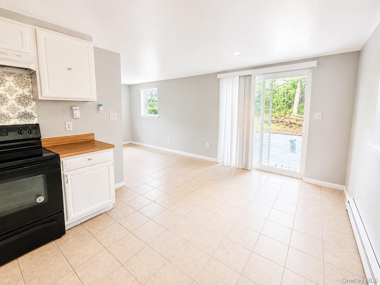 Kitchen area with white cabinetry, wood-finish countertop, and a patterned tile backsplash