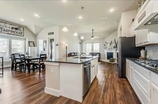 a kitchen with stainless steel appliances granite countertop a stove top oven a sink dishwasher a dining table and chairs with wooden floor