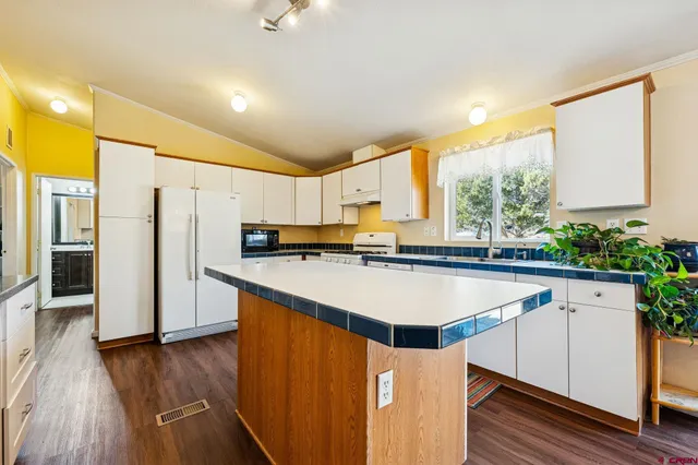 a kitchen with stainless steel appliances granite countertop a refrigerator a sink dishwasher a stove and white countertops with wooden floor