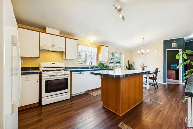 a kitchen with stainless steel appliances a stove a sink dishwasher a refrigerator white cabinets and wooden floor next to a window