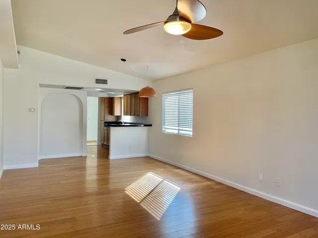 a view of empty room with wooden floor and kitchen