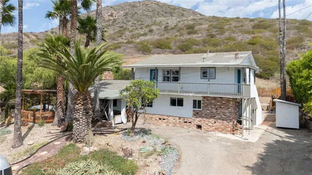 a view of a white house with large trees and wooden fence