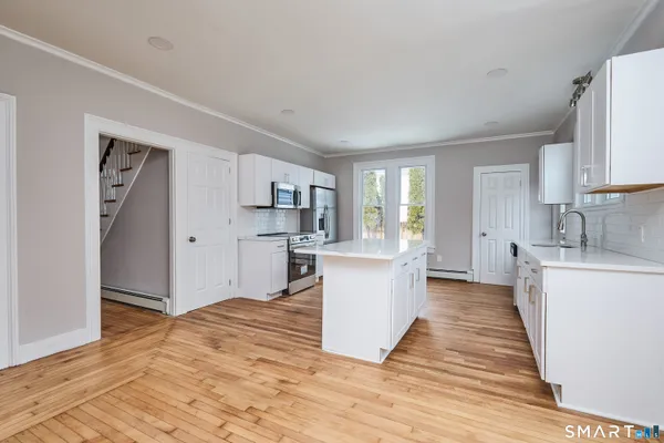 a large kitchen with kitchen island a sink dishwasher stove and white cabinets with wooden floor