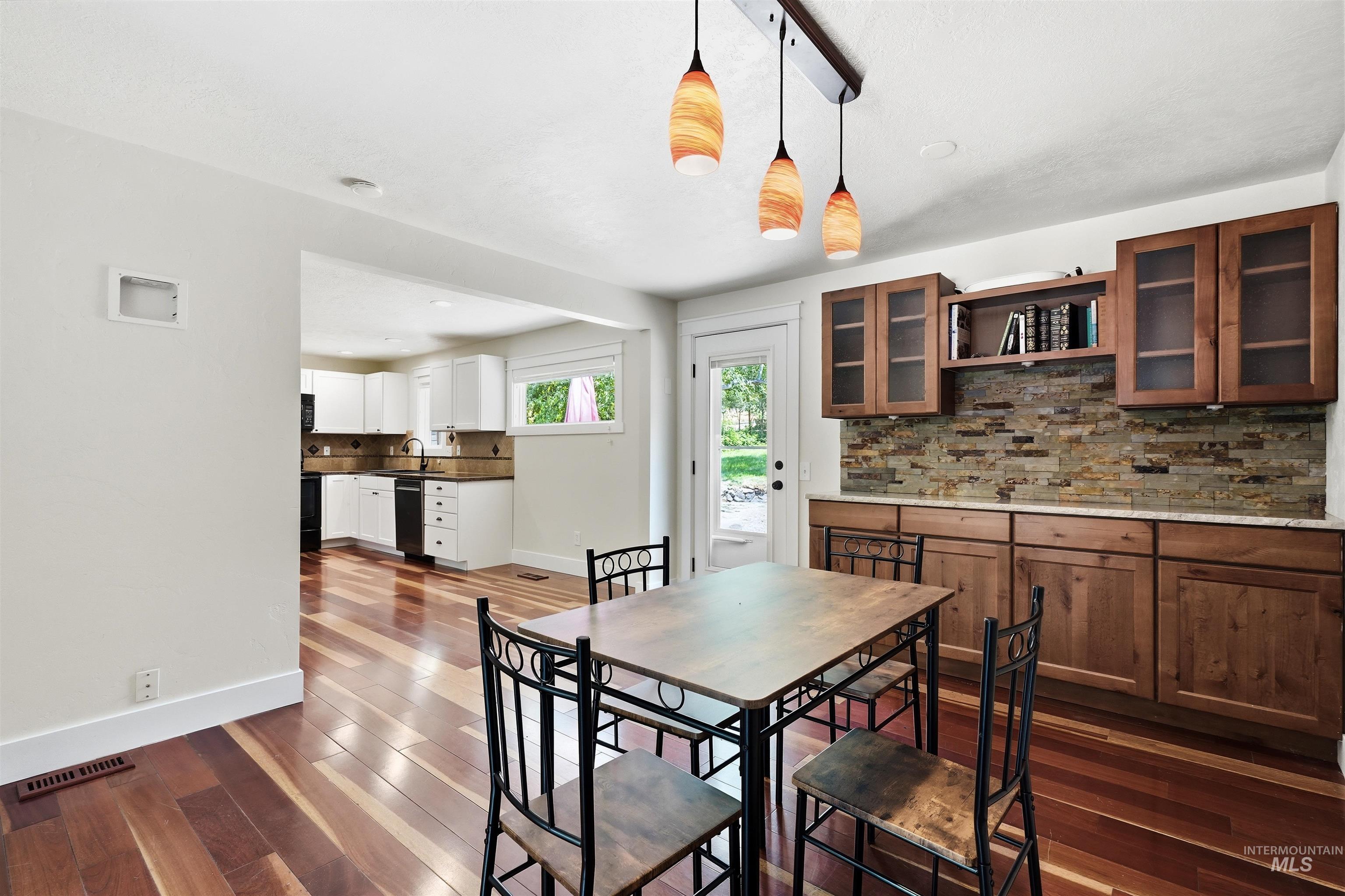 23650 Freezeout Road Caldwell, ID 83607 - Photo 16 of 42 Dining area featuring wood-finish flooring, a wood-finish built-in buffet with glass-front upper cabinetry, and a stacked stone backsplash