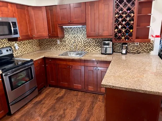 a kitchen with stainless steel appliances granite countertop a refrigerator a stove and a sink with wooden cabinets
