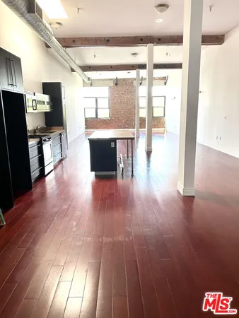 a living room with stainless steel appliances with kitchen view and wooden floor