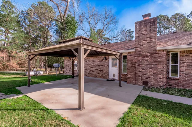 a view of a patio with a table and chairs under an umbrella with large trees