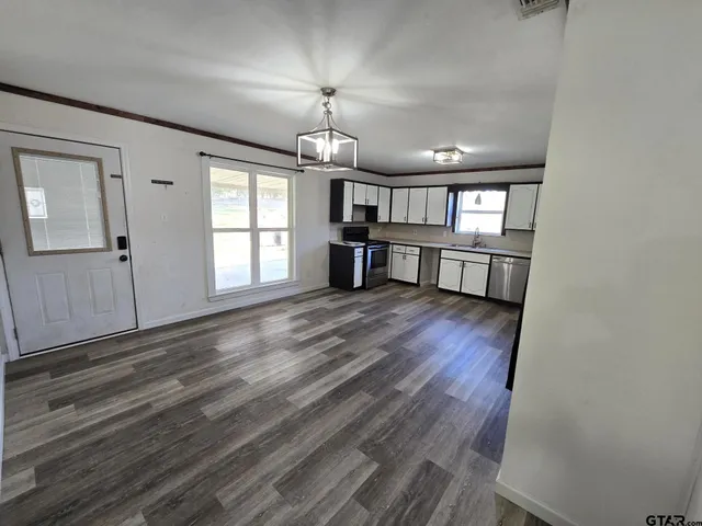 an empty room with wooden floor chandelier and windows