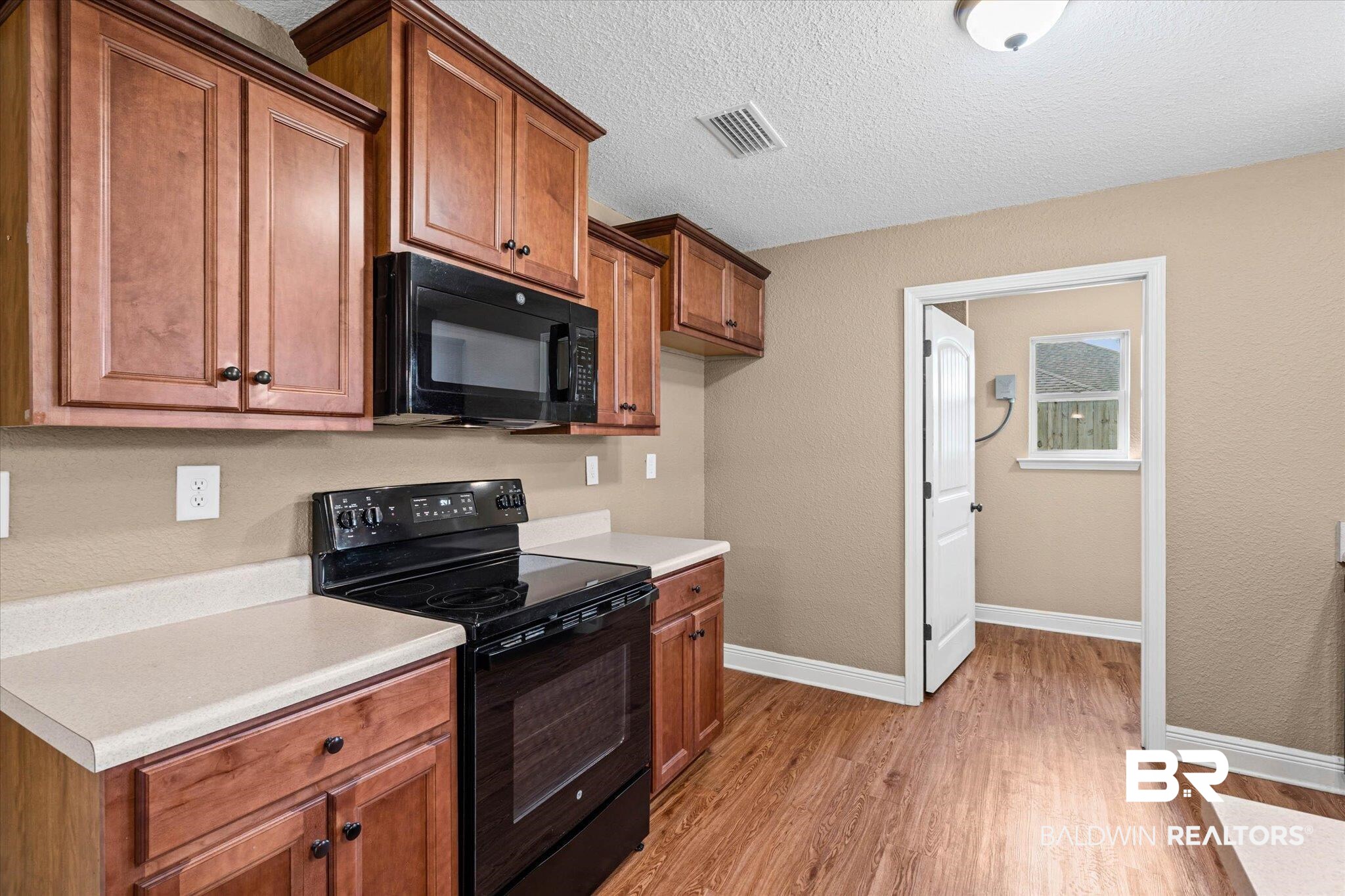 101 Washington Boulevard Foley, AL 36535 - Photo 9 of 32 Kitchen featuring black appliances, wood finish cabinets, a textured ceiling, light countertops, and light wood-style flooring