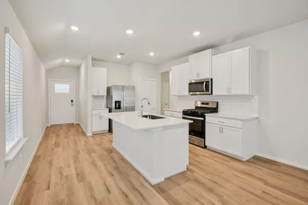 a large kitchen with stainless steel appliances granite countertop a stove top oven a sink dishwasher and a refrigerator with wooden floor