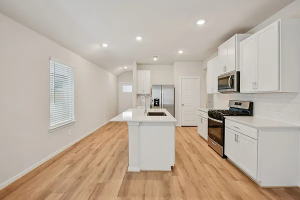 a white kitchen with wooden floor and stainless steel appliances